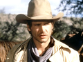 Harrison Ford w kapeluszu i płaszczu, tło górzyste, widok na konie.