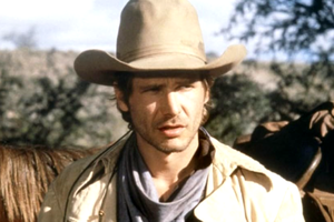Harrison Ford w kapeluszu i płaszczu, tło górzyste, widok na konie.
