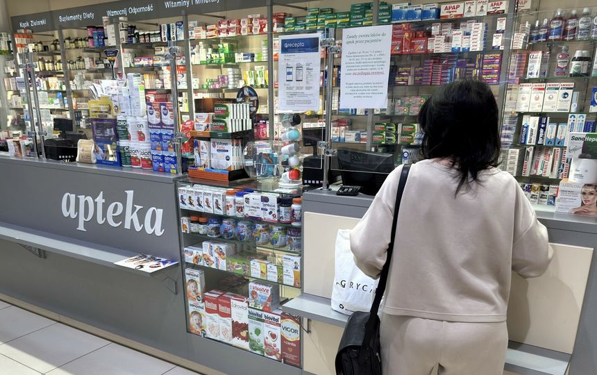 Kobieta w jasnym stroju stoi przy ladzie apteki, otoczonej lekami i suplementami.