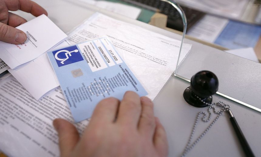 Na stole widoczne dokumenty, w tym karta parkingowa dla osób niepełnosprawnych.