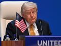 Mężczyzna w garniturze siedzi przy stole z flagą USA, wygląda na zamyślonego.