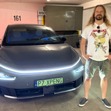 Mężczyzna stoi obok nowoczesnego samochodu w garażu. Na sobie ma koszulkę z logo zespołu Metallica.