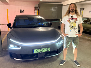 Mężczyzna stoi obok nowoczesnego samochodu w garażu. Na sobie ma koszulkę z logo zespołu Metallica.