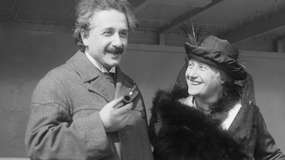Na zdjęciu Albert Einstein z uśmiechniętą kobietą, oboje w eleganckich strojach, wesoło rozmawiają.