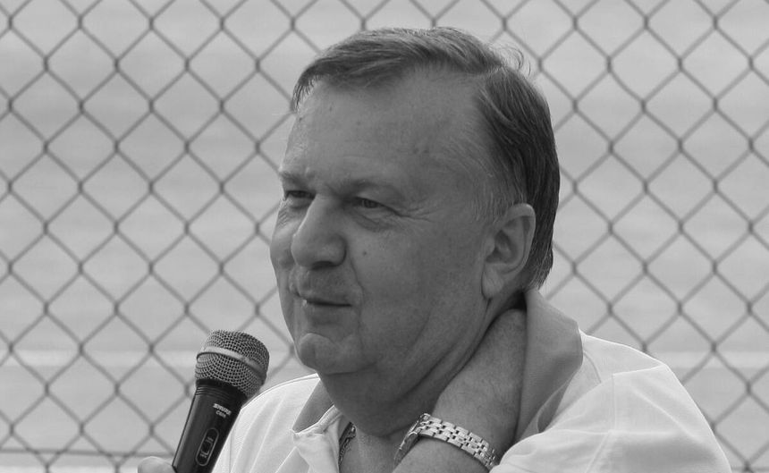 Karol Stopa z mikrofonem, w białej koszuli, mówi do zgromadzenia przy siatce.