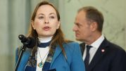 Kobieta z mikrofonem w ręku, w tle mężczyzna w garniturze. Rozmowa w poważnej atmosferze.