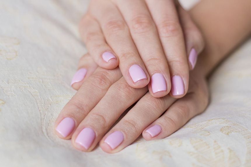 Zbliżenie na ręce z różowym manicurem na jasnym tle. Dłonie złożone na tkaninie.