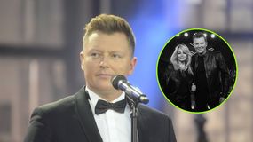 Rafał Brzozowski w garniturze z mikrofonem, na tle sceny.