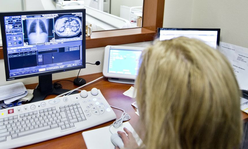 Kobieta siedzi przy biurku, analizując obrazy medyczne na monitorze. W tle widać sprzęt medyczny.