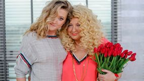 Magda Gessler i Lara Gessler w kolorowych bluzkach trzymają bukiet czerwonych tulipanów.