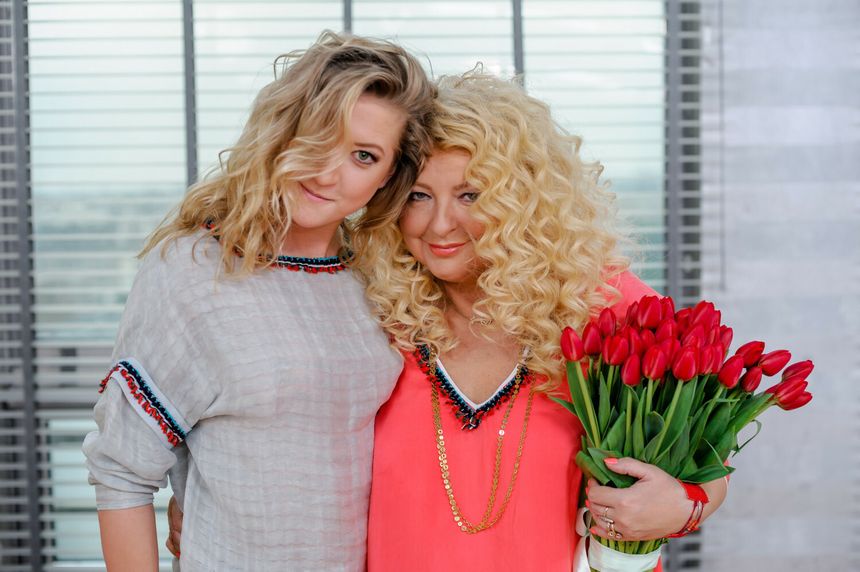 Magda Gessler i Lara Gessler w kolorowych bluzkach trzymają bukiet czerwonych tulipanów.
