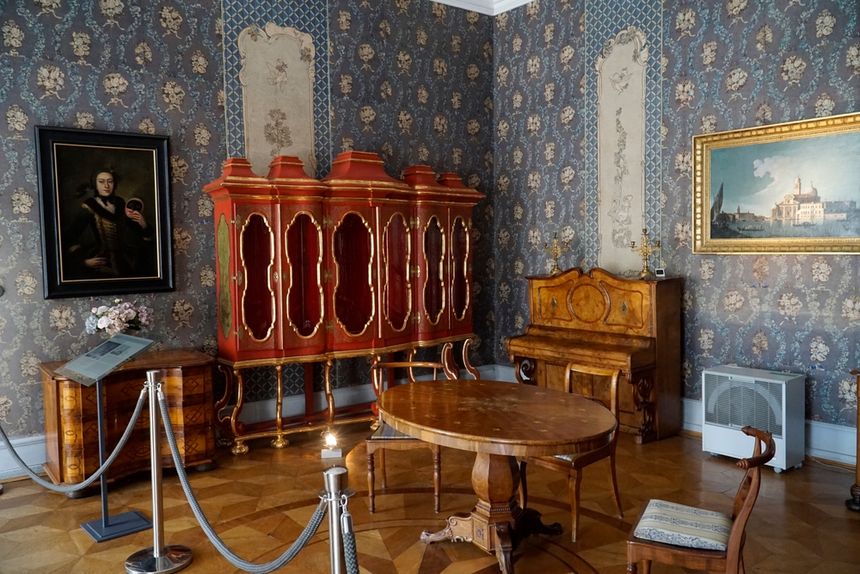 Klimatyczne wnętrze z meblami w stylu historycznym, zdobionymi ścianami i obrazami.