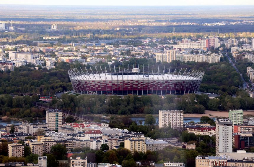 Widok na Stadion Narodowy w Warszawie, otoczony zielenią i urbanistycznym krajobrazem.