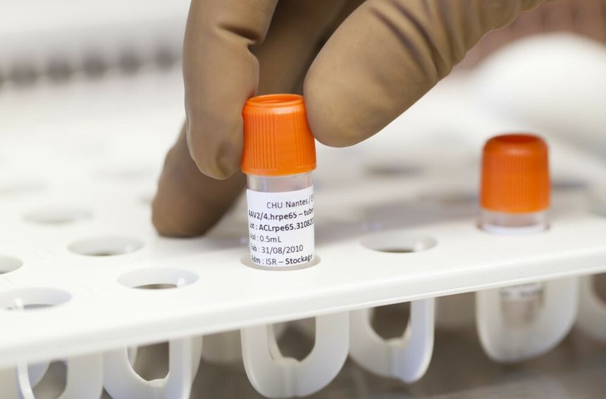 Pracownik laboratoriów trzyma próbkę w fiolce z pomarańczową nakrętką.