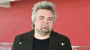 Mężczyzna z siwymi włosami w czarnej kurtce, na tle czerwonej ściany. Nie znam jego tożsamości.