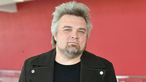 Mężczyzna z siwymi włosami w czarnej kurtce, na tle czerwonej ściany. Nie znam jego tożsamości.
