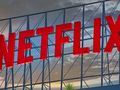 Logo Netflix w czerwonym kolorze, umieszczone na tle nieba z chmurami.
