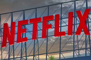 Logo Netflix w czerwonym kolorze, umieszczone na tle nieba z chmurami.