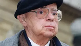 Mężczyzna w okularach i czapce, z poważnym wyrazem twarzy, stoi na zewnątrz.