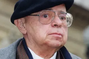 Mężczyzna w okularach i czapce, z poważnym wyrazem twarzy, stoi na zewnątrz.
