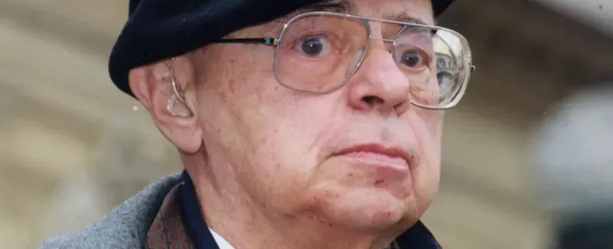 Mężczyzna w okularach i czapce, z poważnym wyrazem twarzy, stoi na zewnątrz.