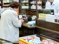 Kobieta w jasnym ubraniu kupuje leki w aptece, rozmawiając z farmaceutą.