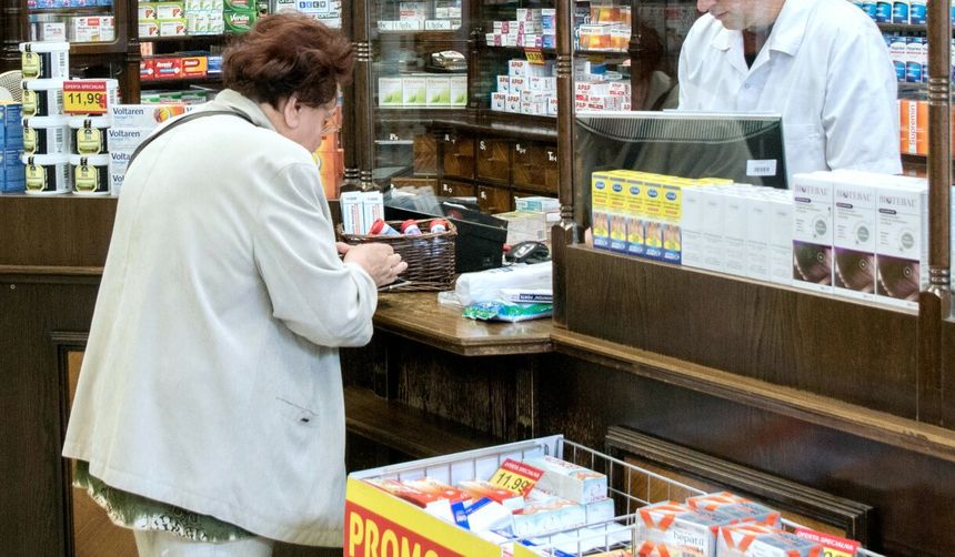 Kobieta w jasnym ubraniu kupuje leki w aptece, rozmawiając z farmaceutą.