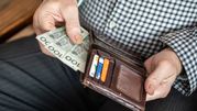 Na zdjęciu widać rękę trzymającą banknoty i portfel z kartami płatniczymi.