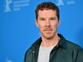 Mężczyzna w jasnej bluzie i ciemnej kurtce stoi na tle niebieskiej ścianki z logo Berlinale.