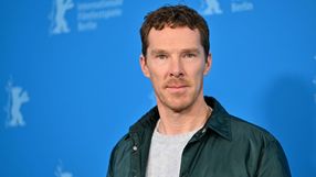 Mężczyzna w jasnej bluzie i ciemnej kurtce stoi na tle niebieskiej ścianki z logo Berlinale.