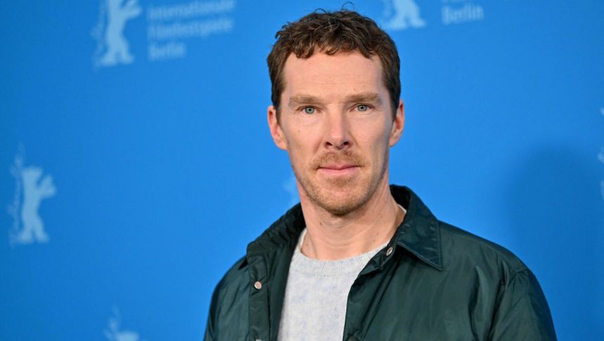 Mężczyzna w jasnej bluzie i ciemnej kurtce stoi na tle niebieskiej ścianki z logo Berlinale.
