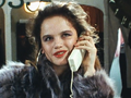 Kobieta w futrze rozmawia przez telefon, z uśmiechem na twarzy, w tle ciemne ubrania.