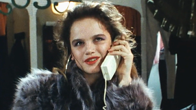Kobieta w futrze rozmawia przez telefon, z uśmiechem na twarzy, w tle ciemne ubrania.