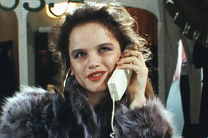 Kobieta w futrze rozmawia przez telefon, z uśmiechem na twarzy, w tle ciemne ubrania.