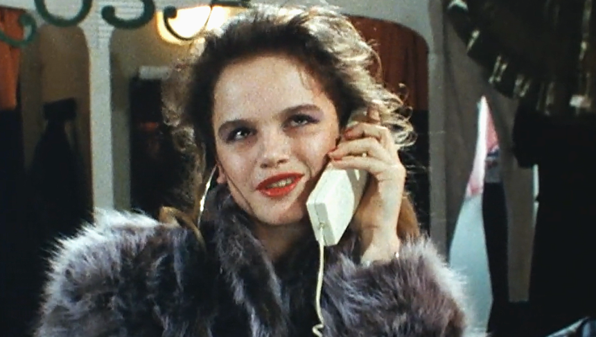 Kobieta w futrze rozmawia przez telefon, z uśmiechem na twarzy, w tle ciemne ubrania.