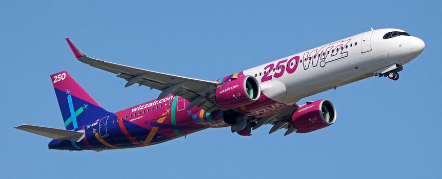 Samolot Wizz Air w kolorowym malowaniu, przelatujący na tle błękitnego nieba.