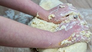 Ręce zagniatają ciasto na blacie, obok widoczne resztki mąki.