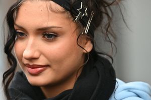 Młoda kobieta z kręconymi włosami, w czarnym szaliku i niebieskiej bluzie, uśmiecha się.