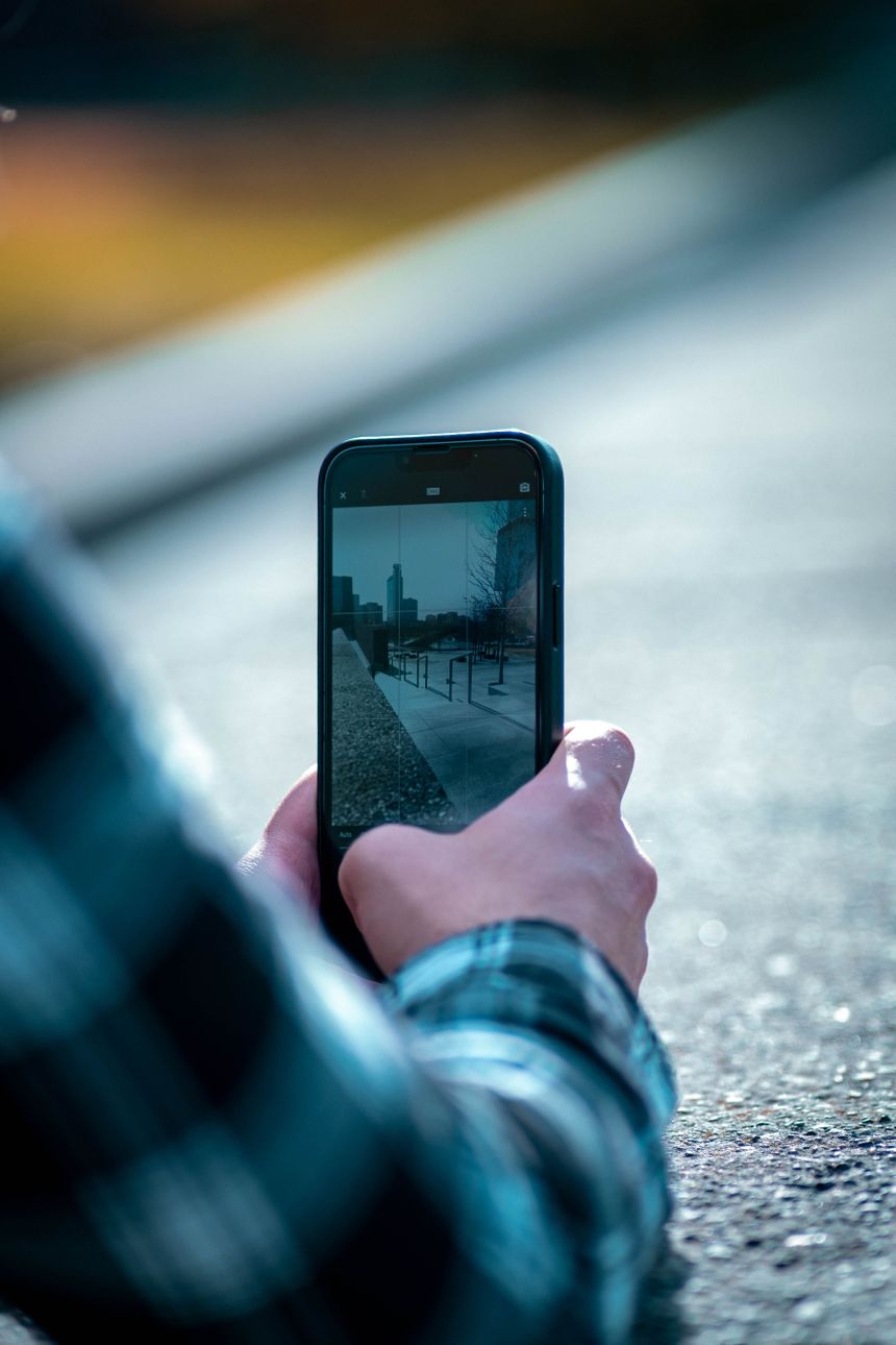 Zdjęcie przedstawia osobę trzymającą telefon, na którym widać krajobraz miejski.