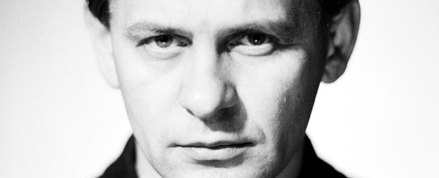 Mężczyzna z poważnym wyrazem twarzy, w czarnej koszuli, na białym tle.
