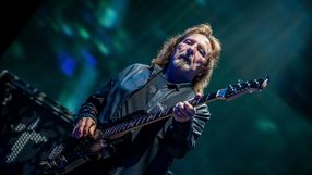 Geezer Butler. Mężczyzna gra na gitarze basowej, w tle kolorowe światła estrady.