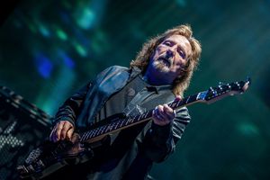 Geezer Butler. Mężczyzna gra na gitarze basowej, w tle kolorowe światła estrady.