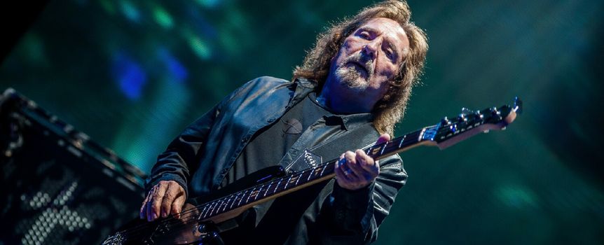 Geezer Butler. Mężczyzna gra na gitarze basowej, w tle kolorowe światła estrady.