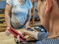 Osoba płaci w sklepie, trzymając czerwoną portmonetkę; w tle widać chleb i kasę.