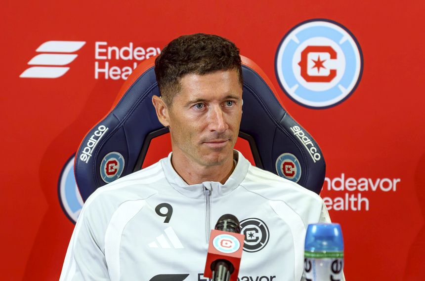 Na zdjęciu Robert Lewandowski podczas konferencji prasowej. Tło w kolorze czerwonym, siedzisko sportowe.
