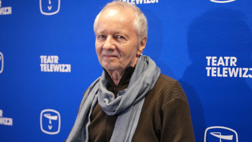Mężczyzna w szarej chustce na tle niebieskiego banera 