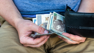 Ręka trzymająca banknoty w portfelu, na tle spodni w kolorze beżowym.