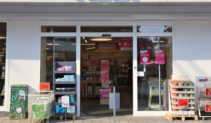Wejście do sklepu z kolorowymi reklamami oraz regałami z artykułami gospodarstwa domowego.