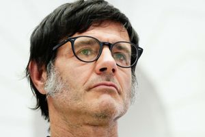 Mężczyzna z okularami, z krótkimi włosami i zarostem, patrzy w dal w jasnym otoczeniu.