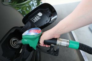Osoba tankująca paliwo, trzyma pistolet wlewu przy czarnej karoserii samochodu.